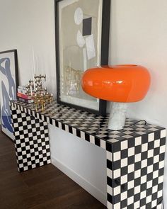 an orange lamp sitting on top of a black and white checkerboard table next to a mirror