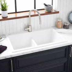 a white kitchen sink sitting under a window next to a potted plant on a counter