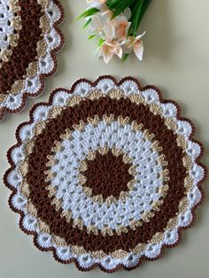 two crocheted coasters sitting on top of a table next to a bouquet of flowers