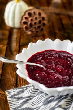 a white bowl filled with cranberry sauce on top of a wooden table next to pumpkins