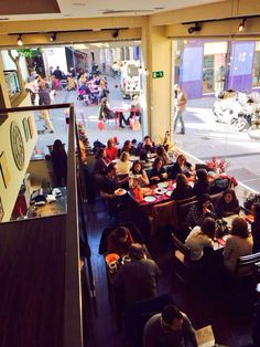 people sitting at tables in a restaurant with large windows looking out on the street and pedestrians walking by