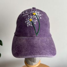 a purple hat with dandelions embroidered on it sitting on a mannequin head