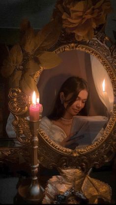 a young woman reading a book in front of a mirror with two candles on it