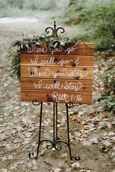 a wooden sign with writing on it sitting in the leaves next to a road and trees