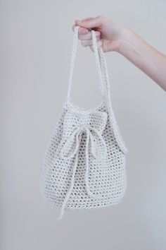 a hand holding a white crocheted bag with a knot on the front and side