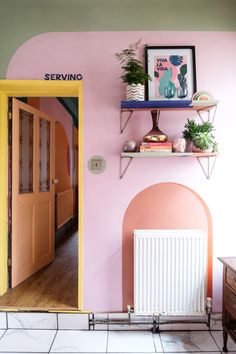 a pink and green room with a yellow door in the corner, shelves on the wall and a radiator