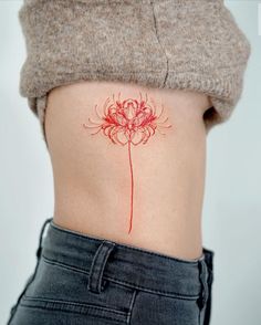 a woman's stomach with a red flower tattoo on her left side ribcage