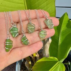 a person is holding four pieces of green sea glass in their palm leaf necklaces