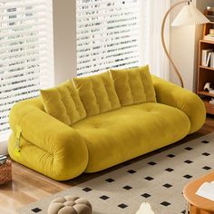 a yellow couch sitting on top of a rug in a living room next to a window