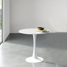 a white table sitting in front of a window next to a bowl on top of a plate