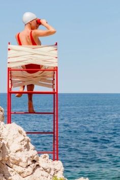 a man sitting on top of a lifeguard chair next to the ocean with his head in his hands