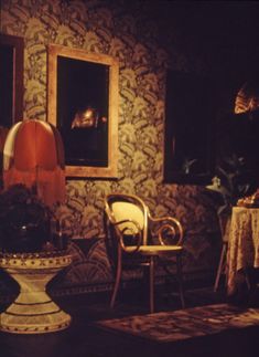 two chairs and a table in a dimly lit room with paintings on the wall behind them