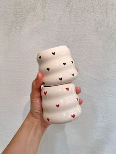 a hand holding three ceramic cups with hearts on them