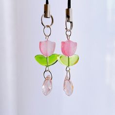 a pair of pink and green flower earrings hanging from a hook on a white wall