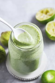 a glass jar filled with green smoothie next to limes