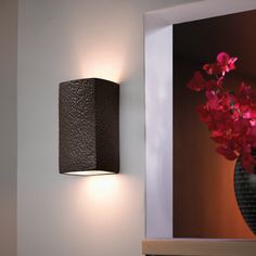 a wall mounted light next to a vase with red flowers in it and a mirror on the wall