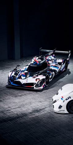 two race cars are shown side by side in the dark, one is white and the other is blue