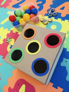 a cardboard box filled with lots of different colored balls next to some scissors and other toys