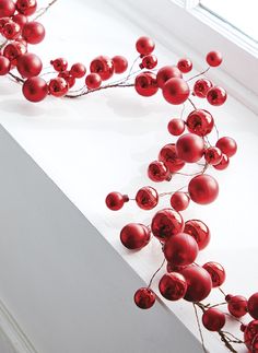 some red berries are hanging on a window sill in front of a white wall