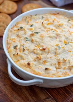 a casserole dish with cheese and crackers in the background on a wooden table