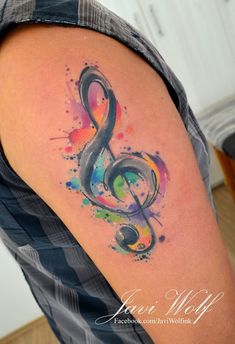 a colorful tattoo with a musical note on it's left arm and watercolor paint splatters