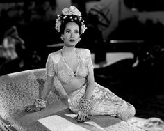 a woman sitting on top of a couch wearing a dress and headpiece with flowers in her hair