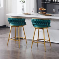 two green velvet stools sitting in front of a counter