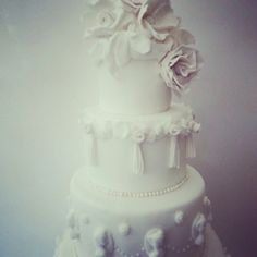 a three tiered white wedding cake with flowers on the top and pearls around the edges