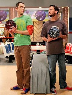 two men standing next to each other with bowling balls in their hands and one holding a ball