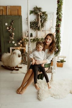 a woman sitting on a swing with her child in front of christmas decorations and garlands