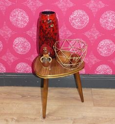 a red vase sitting on top of a wooden table next to a pink wall with circles