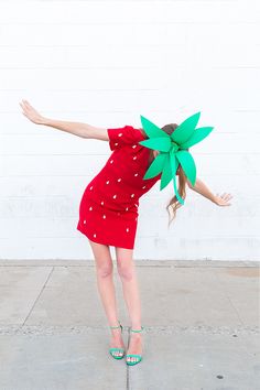 a woman in a red dress is holding up a green paper flower on her head