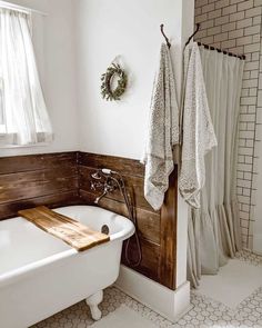 a white bath tub sitting under a window next to a wooden shelf filled with towels