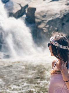 a woman standing in front of a waterfall taking a photo with her cell phone while wearing a headband