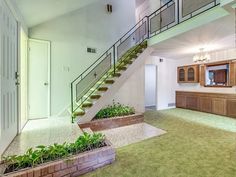 an empty living room with stairs leading to the second floor and green carpeted floors