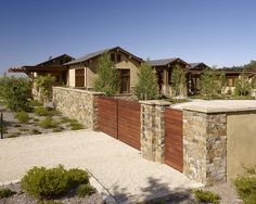 a house with stone walls and wooden gates in the front yard, surrounded by greenery