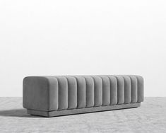 a long gray couch sitting on top of a cement floor next to a white wall