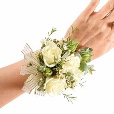 a woman's hand holding a bouquet of white roses and greenery on her wrist