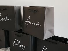 four black shopping bags with white writing on them are stacked up against the wall in front of each other