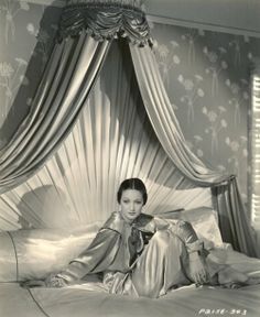 a woman laying on top of a bed in a room with curtains and drapes