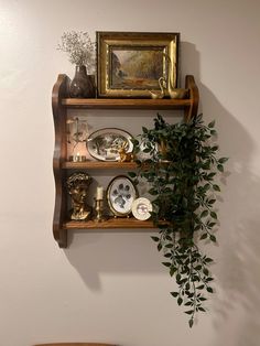 a wooden shelf with plants and plates on it next to a wall mounted framed painting