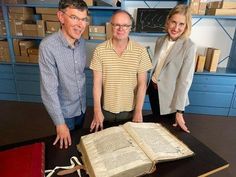 three people standing next to an open book on a table in a room with blue cabinets