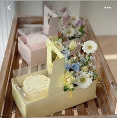 three boxes with flowers in them sitting on a wooden table next to some cakes and cookies