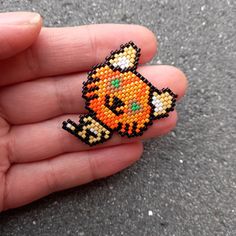 a hand holding a small beaded brooch with an orange cat on it's back