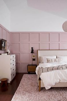 a bedroom with pink walls and white bedding in front of a wooden chest of drawers