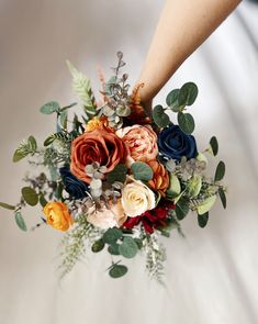 a bridal bouquet being held by someone's hand with foliage and flowers on it