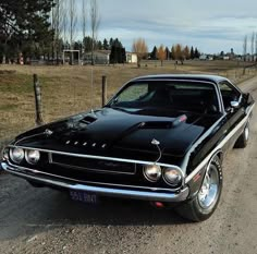 an old black car parked on the side of a dirt road in front of a fence