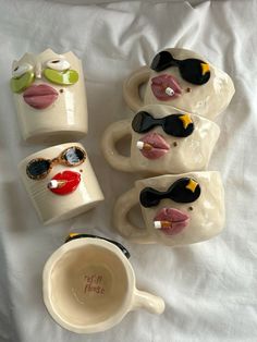 four mugs with faces painted on them are sitting next to each other in front of a white sheet