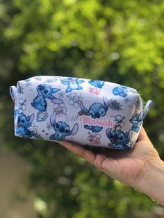 someone is holding up a small bag with stitchy characters on it in front of some trees