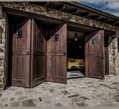 two wooden doors open in front of a stone building with a yellow car parked behind them